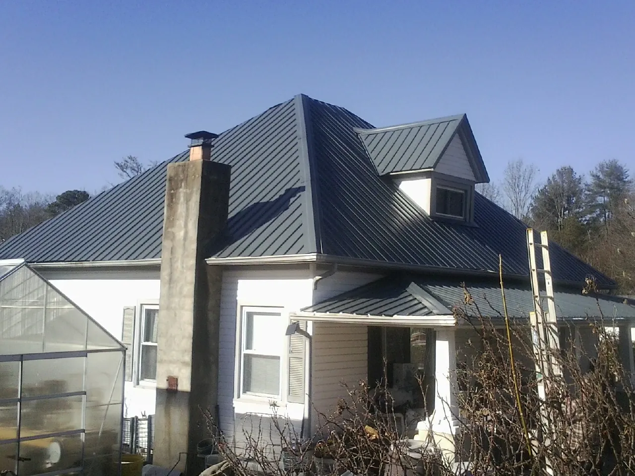 Dark blue standing seam metal roof on a white farmhouse with dormer — Slate & Tile Roof Repair by Roofing Brothers in Mitchellville