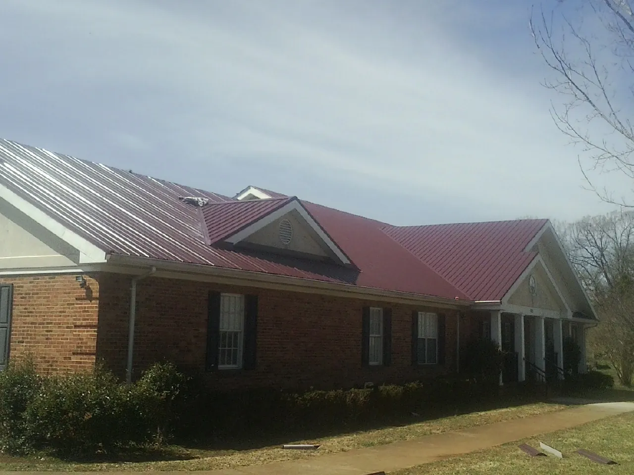 Red metal roof with gabled entries on a long brick building, from a Hail Damage Roof Repair job in Mitchellville