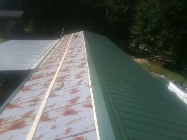 Old rusted panels beside newly installed green metal roofing — Wind Damage Roof Repair by Roofing Brothers in Mitchellville