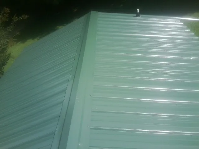 New green metal panels meeting at the ridge of a roof — Flat Roof Repair work by our crew in Mitchellville