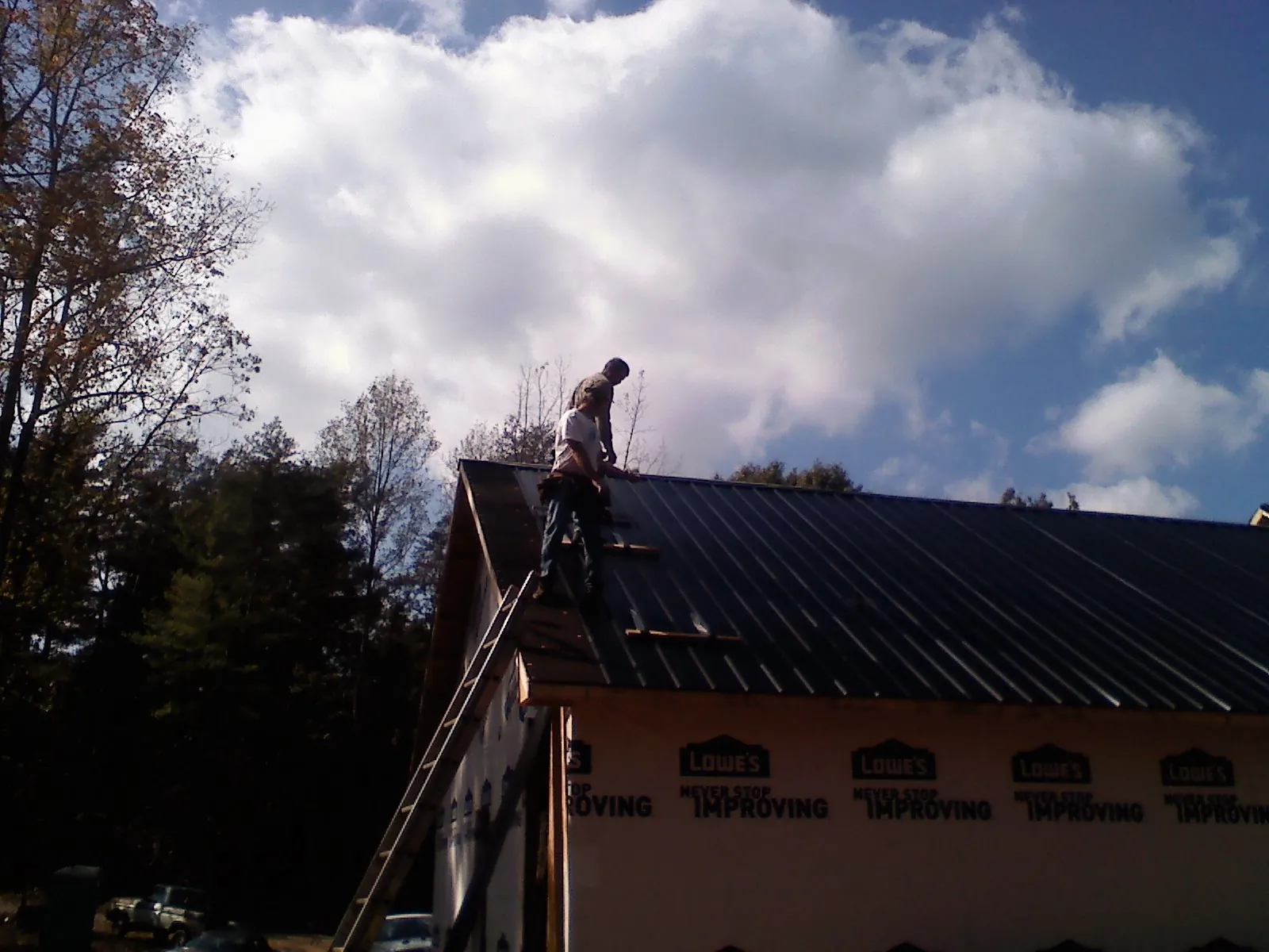 Roofer fastening dark metal panels high against a cloudy sky, from a Roof Inspection job in Mitchellville
