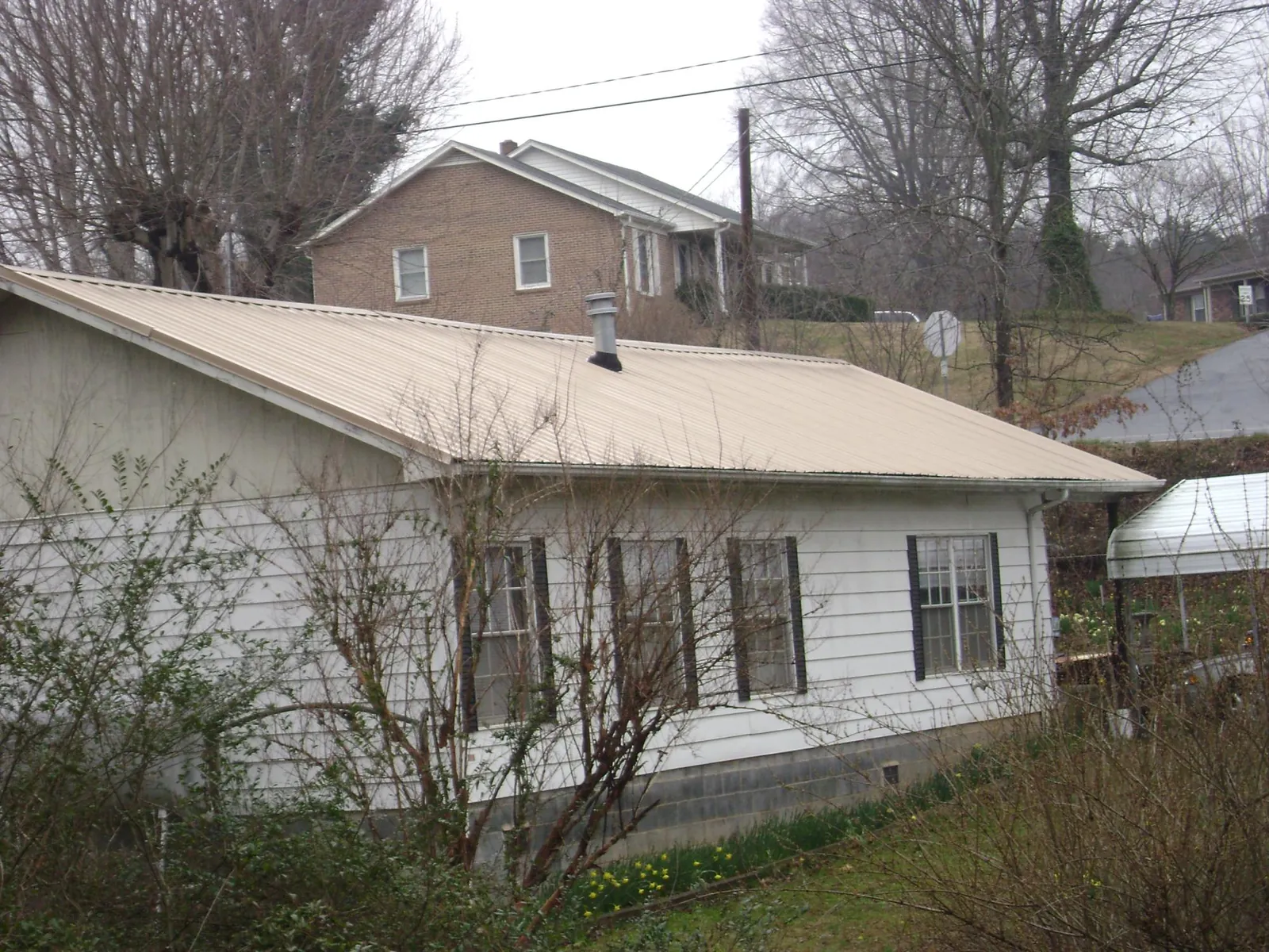 Tan metal roof on a white sided house set into a hillside — Commercial Roofing by Roofing Brothers in Mitchellville